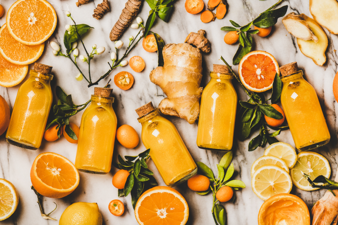 Flat-lay of fresh turmeric, ginger, citrus juice shot in glass bottles over marble background