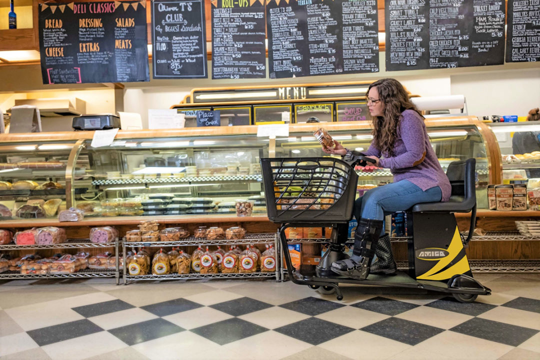 grocery-shopper-in-electric-wheelchair-in-deli-section-of-a-supermarket-holding-a-product-and-reading-the-package