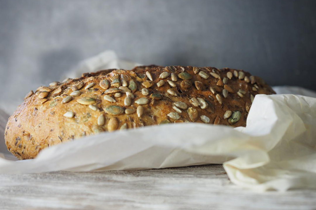 loaf-of-whole-grain-bread-in-white-paper-with-gray-background