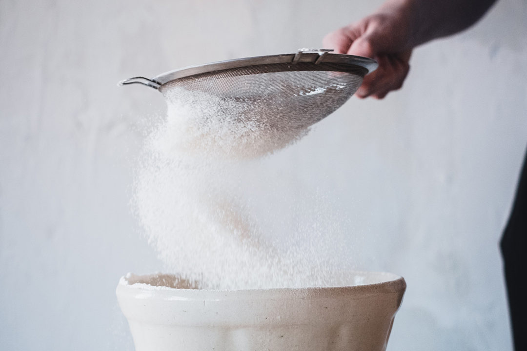 hand sifting sugar into a bowl