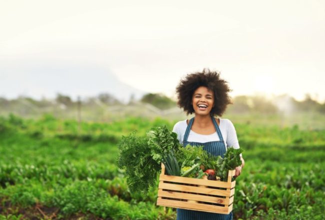 woman smiling in a field holding a box of vegetables