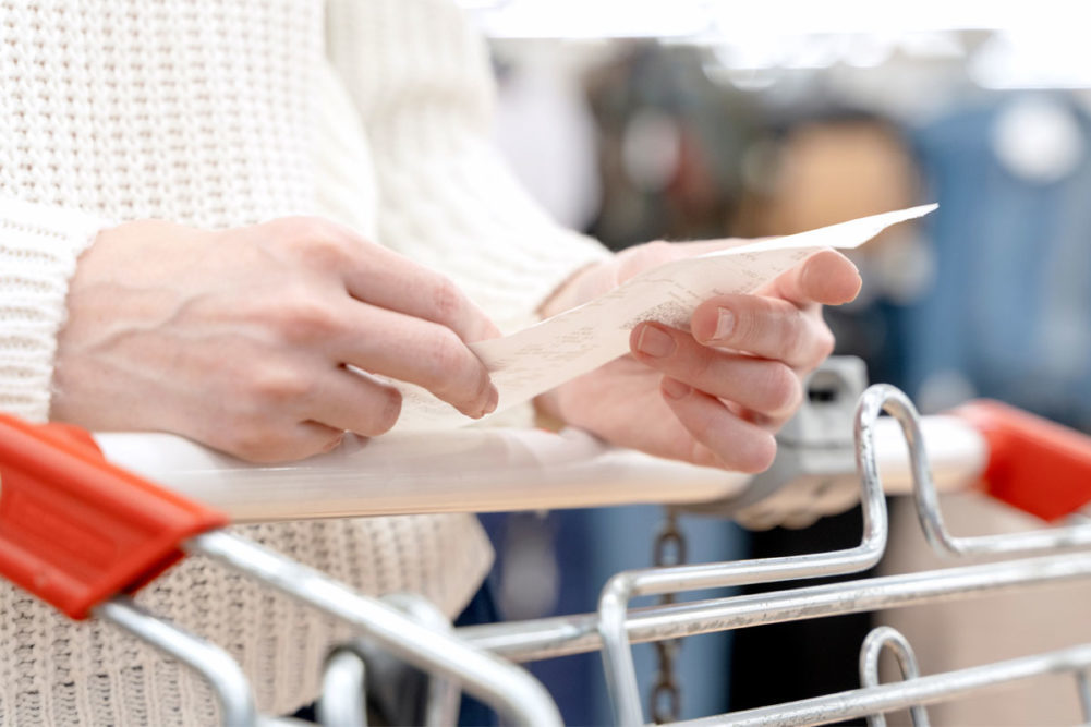 hands holding receipts and resting on a shopping cart