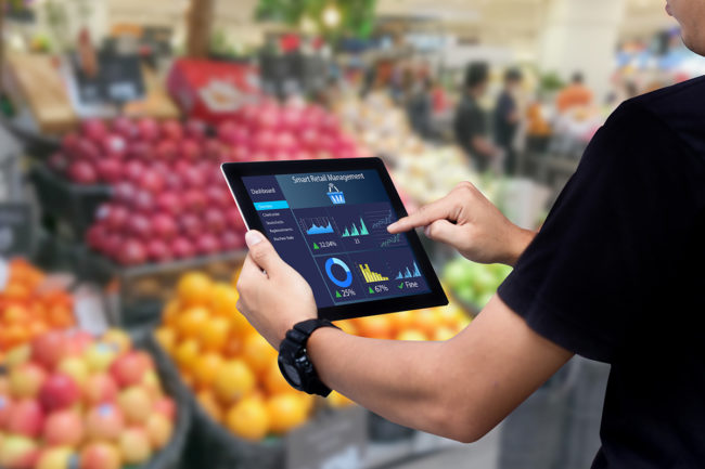 Smart retail management system. Worker hands holding tablet on blurred supermartket as background
