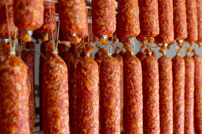 Dried sausage hanging on a rope on a metal frame in the smoke house