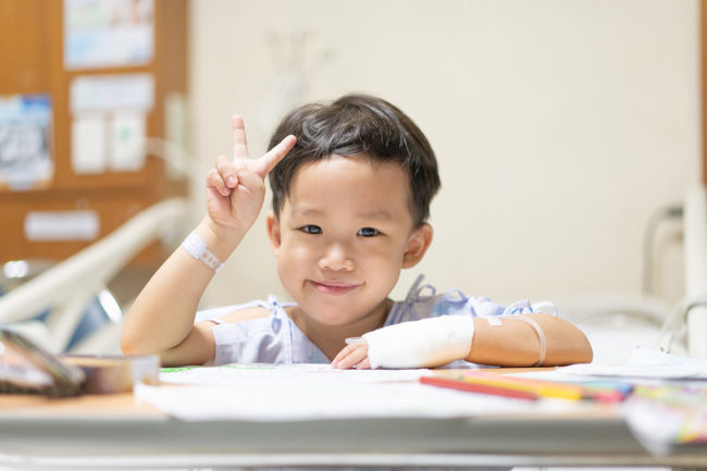 smiling child in a hospital holding up a "peace" sign with two fingers