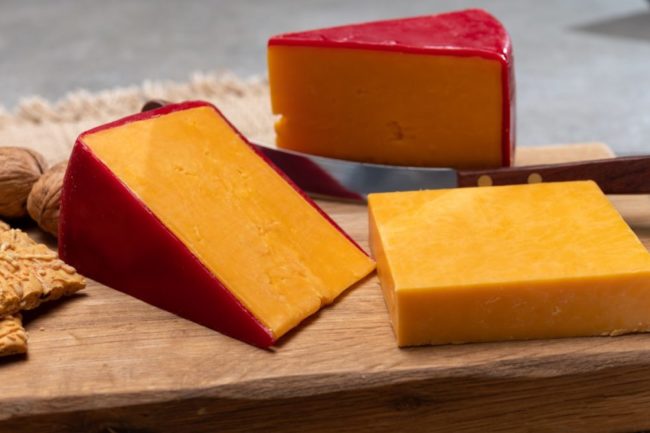 wedges of orange cheese with red wax on a wooden board