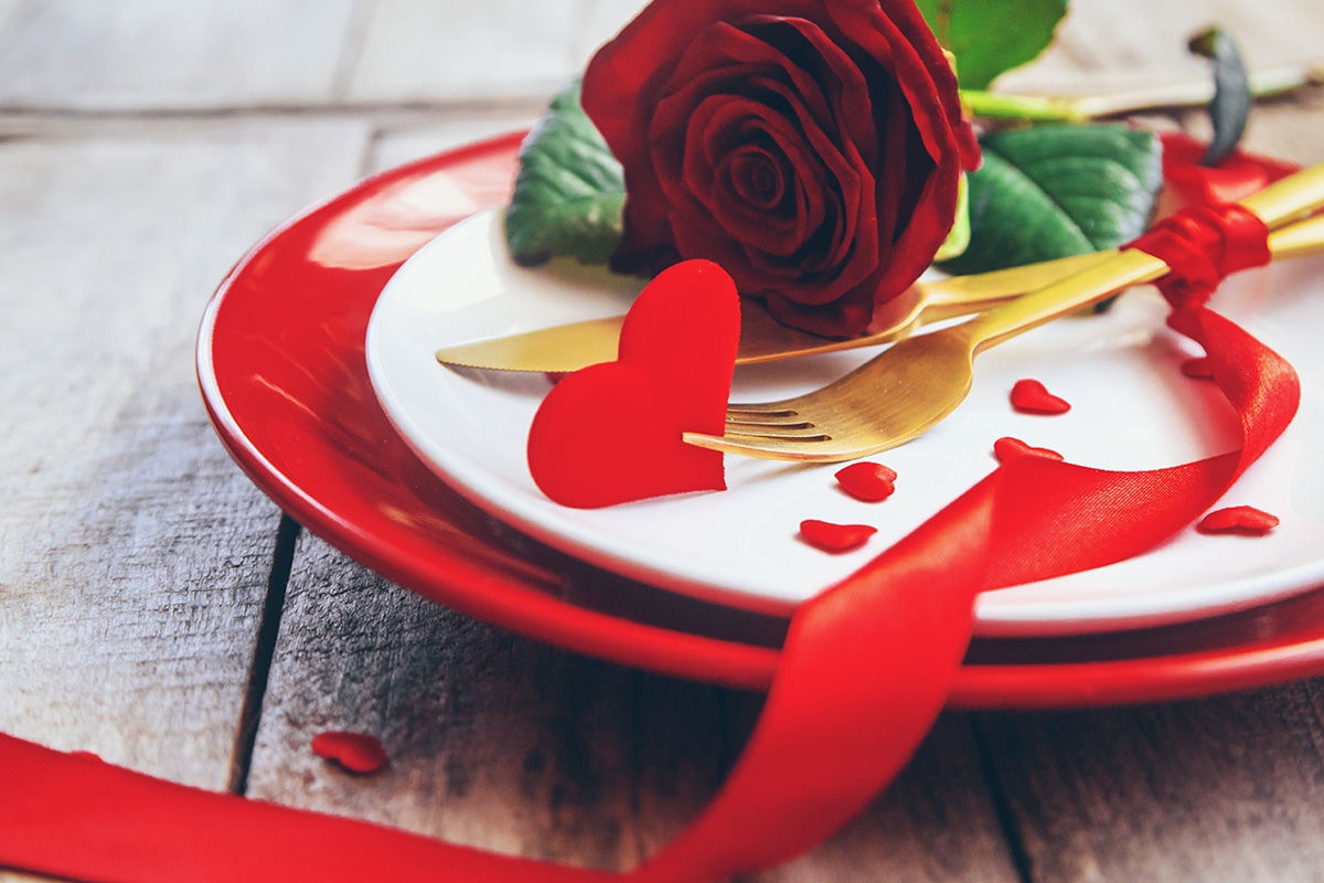 plates and silverware on a table with a red rose and heart cut-outs