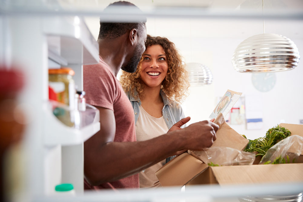 View looking out from inside of a refrigerator as a couple unpacks a meal kit