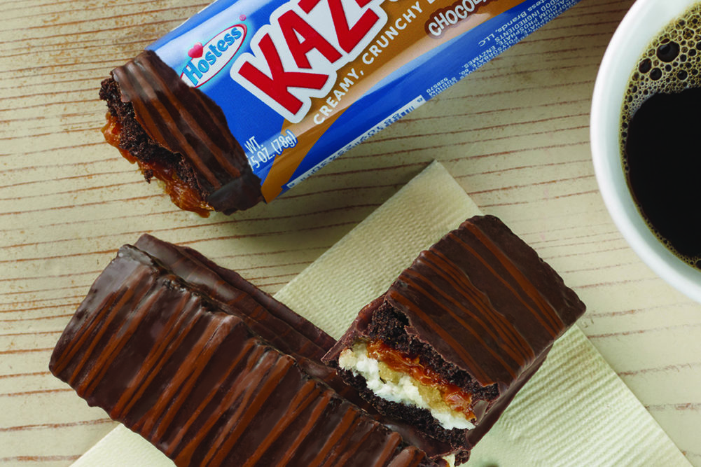 Hostess Chocolate Caramel Kazbars on a wooden surface with a cup of coffee in the corner