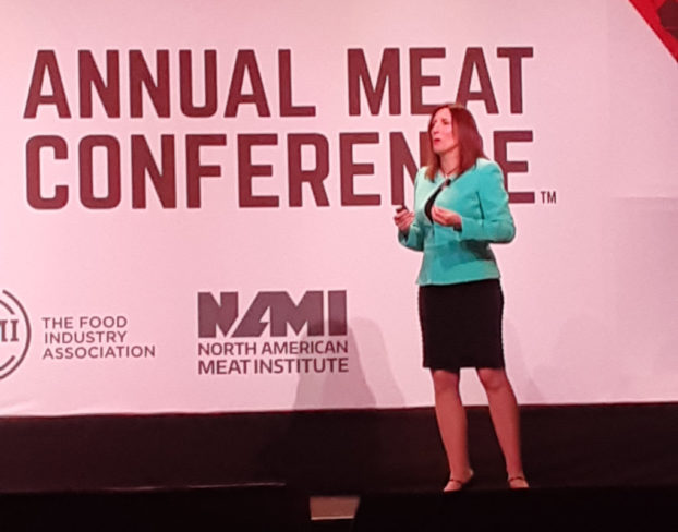 Woman speaking on stage with an annual meat conference screen behind her