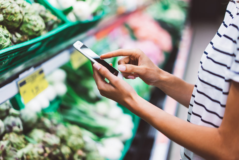 woman's hands holding a smart phone in a grocery store produce aisle