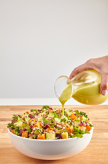 avocado salad in a white bowl with a hand pouring a salad dressing over it