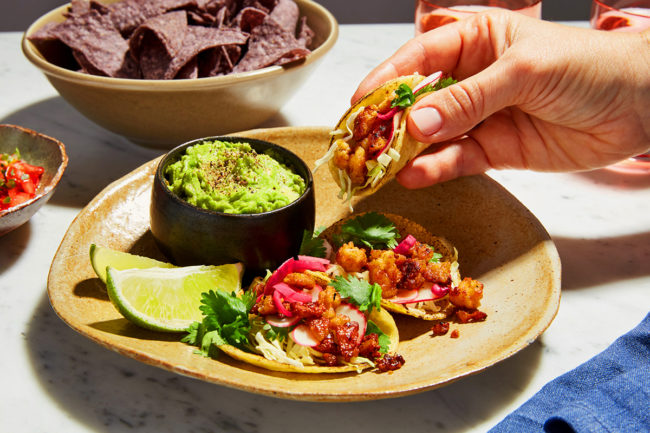 Small tacos on a plate with a hand picking one up