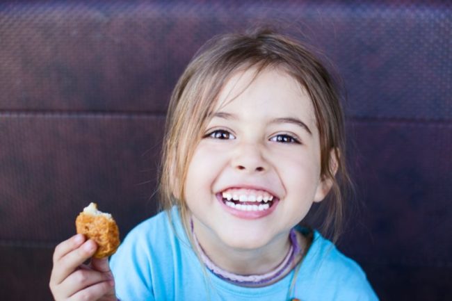 child holding a chicken nugget and smiling