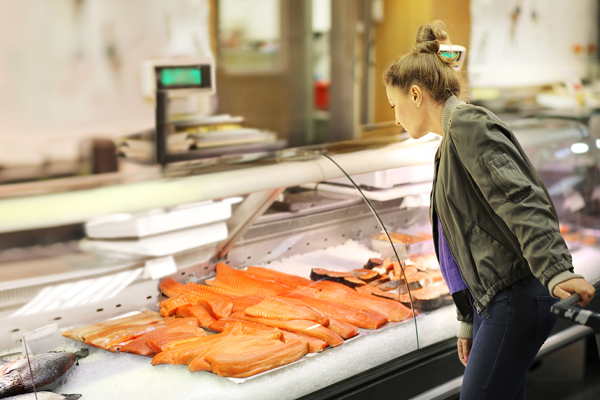 Woman shopping for fresh fish seafood in supermarket retail store