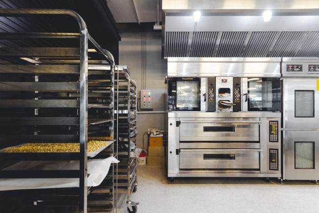 Modern pastry kitchen decorated in black, white and steel with baking machine, oven, conveyor, production line, mixer and cooling plant