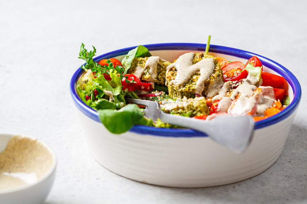 Falafel salad with baked vegetables, tahini dressing and tomatoes in a white bowl. Israeli street food concept.