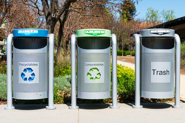Modern multi color bins to collect recyclables, compostables and trash set up outdoor in public place.