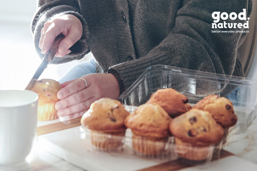 woman's hands slicing a muffin with a knife next to a plastic box of muffins