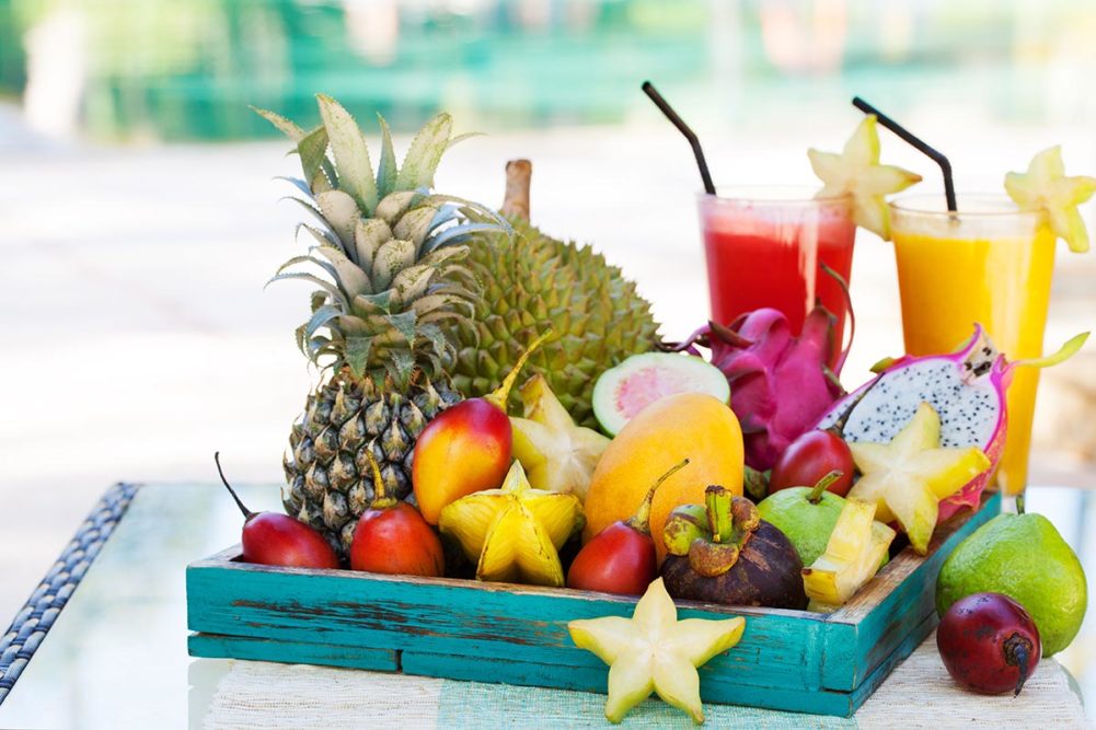 Assortment of tropical exotic fruits with smoothie and fresh juice on a tropical outdoor background