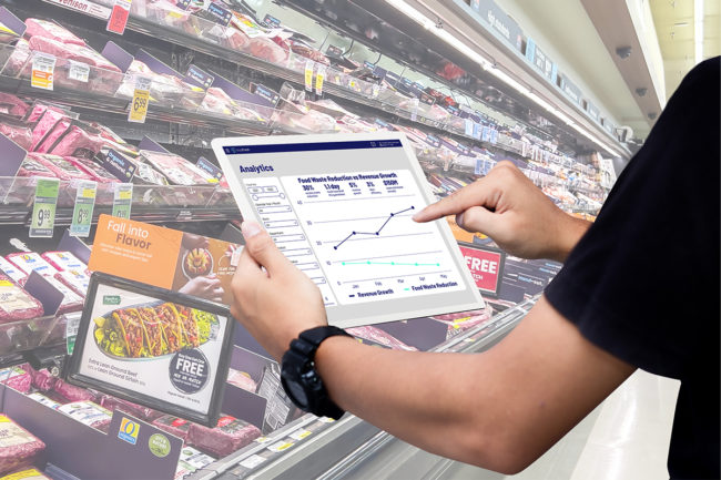 arms holding a tablet with a graph on the screen in the middle of a supermarket