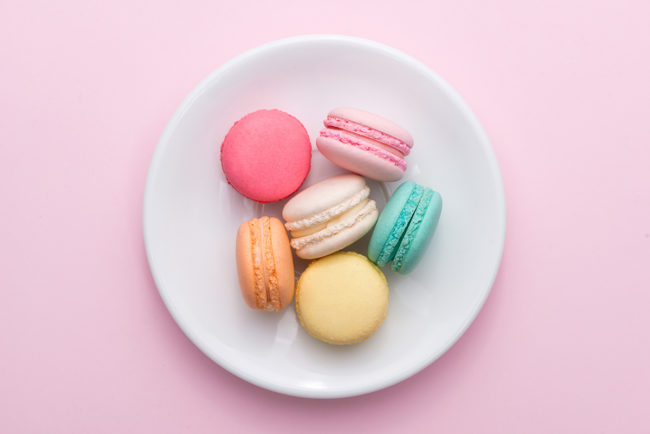 macarons in pastel colors on a white plate with a pink background