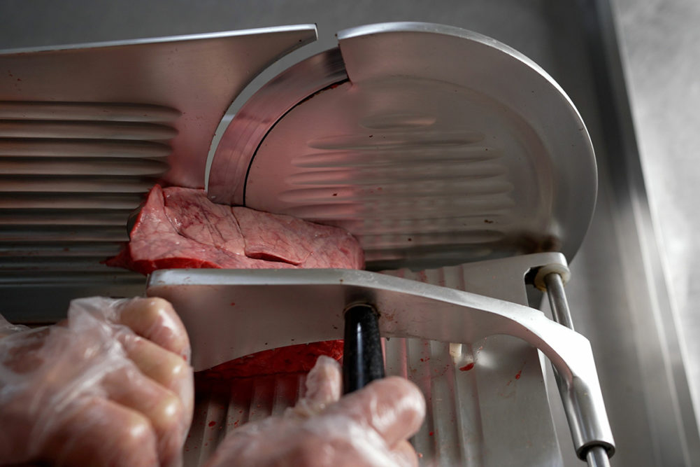 Cutting meat on the machine. Modern semi-automatic electric frozen meat cutting machine for food processing on the table. Hands cut bacon in a slicing machine.