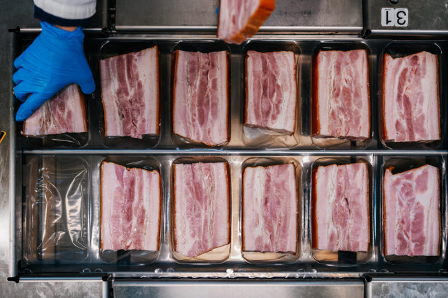 Production line for packing and vacuuming delicious pork meat bacon into small packages. Meat food industry work.