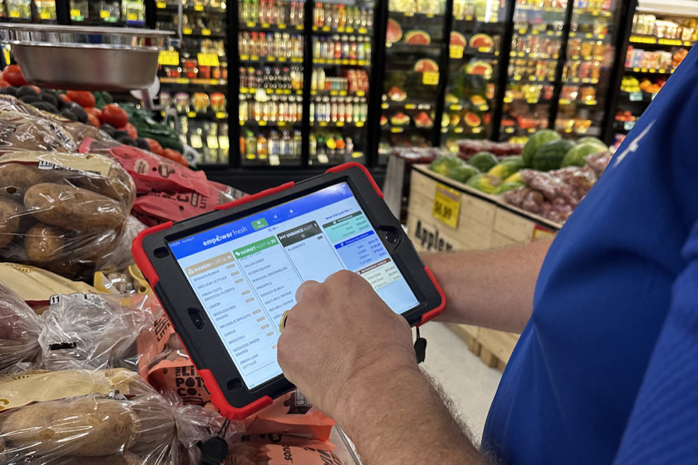 person's hand holding a tablet in a produce department at a grocery store