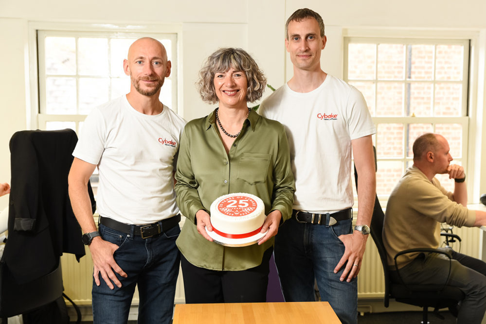 Three Cybake employees standing with a "25 years of Cybake" cake