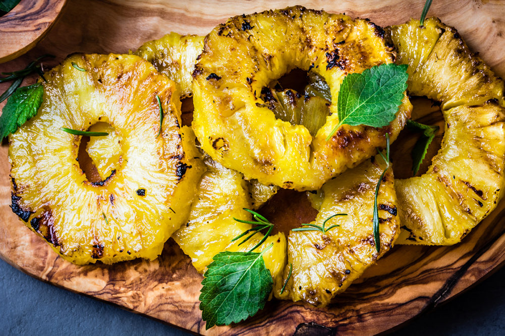 Grilled pineapple slices with mint on olive wooden board. top view
