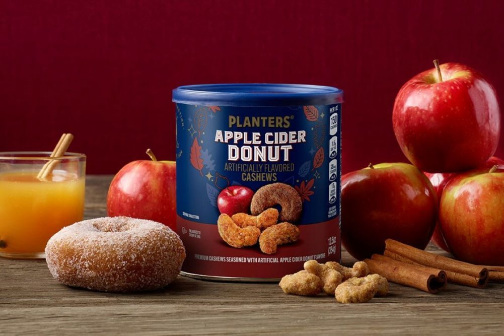 Planters Apple Cider Donut Cashews container with apples and donuts around it on a wooden surface