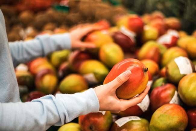 Young woman choose fresh mango at supermarket, hand close up.