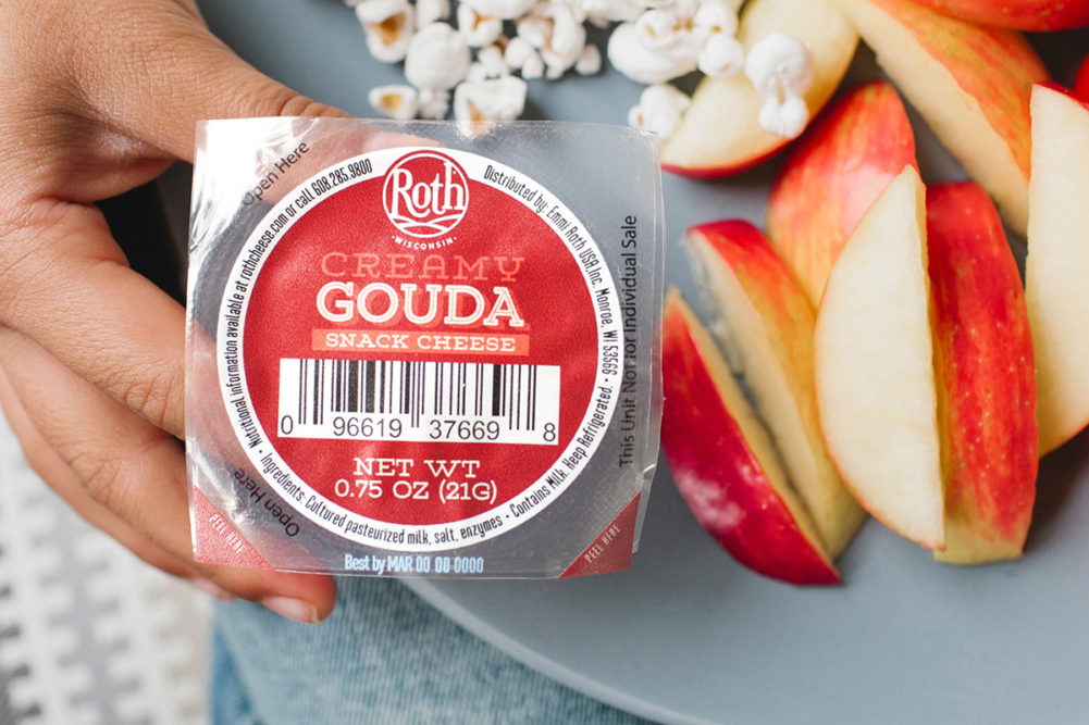 Emmi Roth creamy gouda package held next to a plate of apple slices and popcorn 
