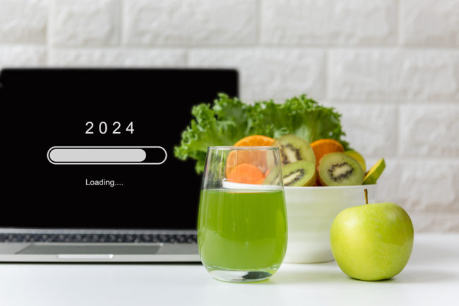 laptop with 2024 loading bar on screen. Bowl of green fruits and cup of green juice next to laptop