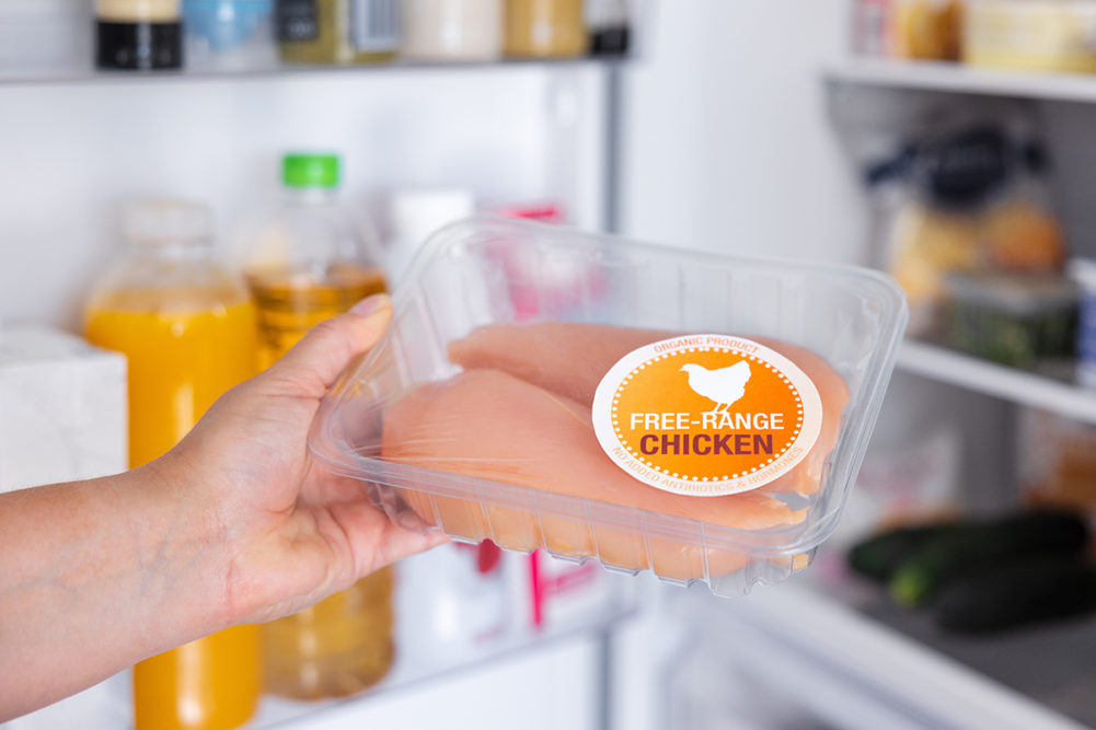 hand holding clear plastic package of raw chicken with "free-range chicken" label