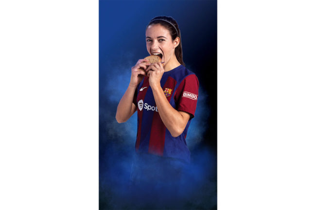 Aitana Bonmatí in a soccer jersey eating a slice of bread