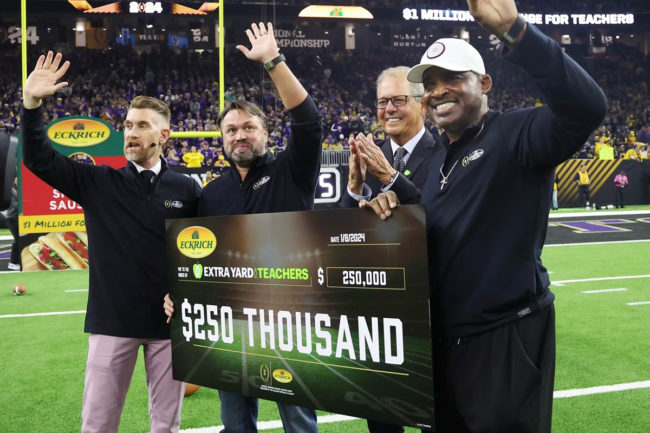 Four people holding a giant check for $250,000 on a football field